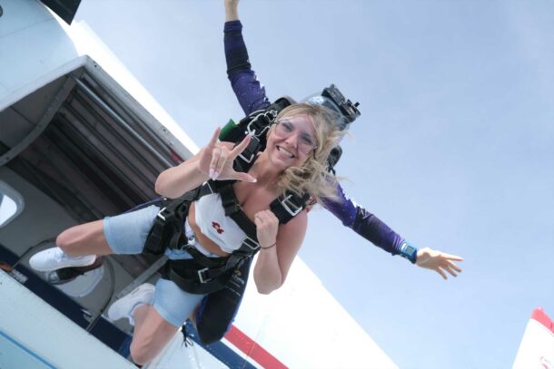 Blonde girl with a tandem instructor exiting the airplane on a tandem skydive.
